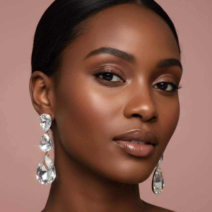 Woman wearing A pair of dangling teardrop rhinestone earrings photographed on a blush background.