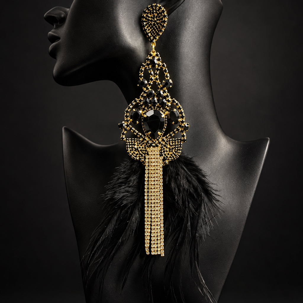 A single large statement earring displayed on a black mannequin bust. The earring has an ornate gold-toned top and mid-section with black inlay details, and a long dangling tassel made of small gold-toned beads or rhinestones.
