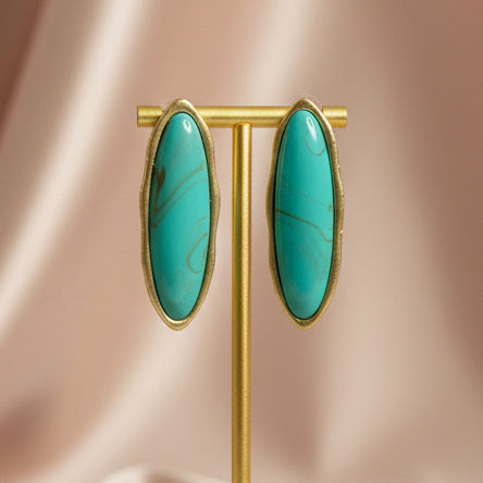 Gold earring stand with turquoise earrings against a beige background
