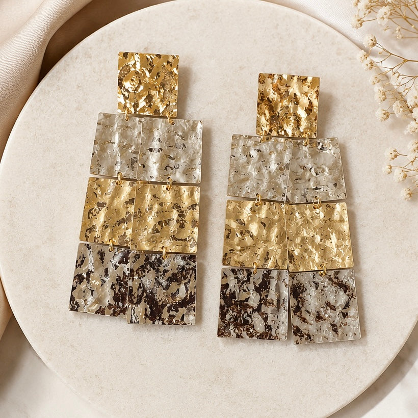 Pair of gold and silver earrings on a round beige stone surface with a soft background.