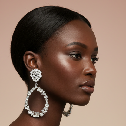 A close-up side profile of a woman with dark hair wearing a large silver teardrop dangle earring set with clear crystals, against a solid beige background.