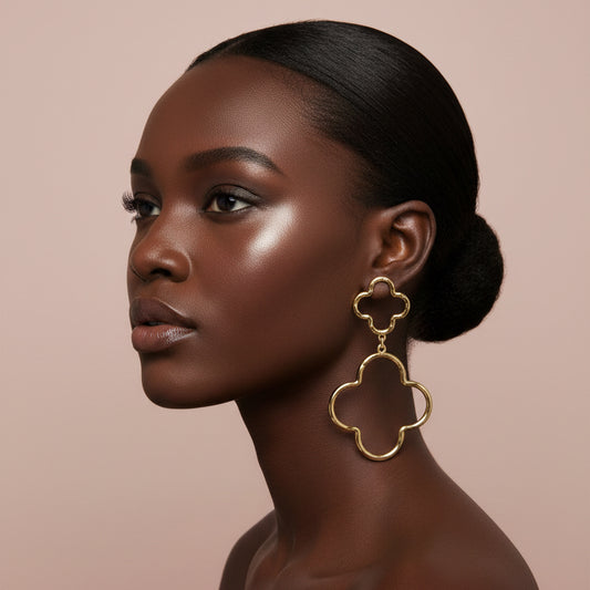 Woman wearing gold Oversized Hammered Metal Open Double Quatrefoil Link Earrings against beige background