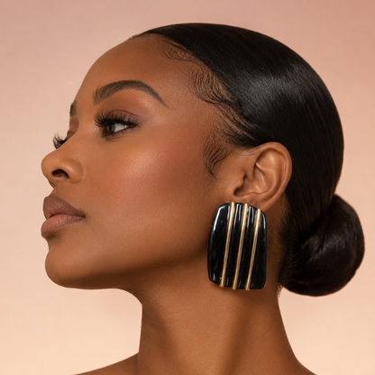 A woman in profile wearing large rectangular drop earrings with black and gold vertical stripes, set against a soft peach background.
