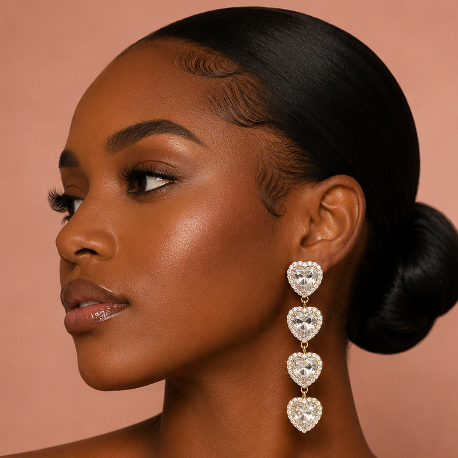 A woman wear heart linked rhinestones dangle earrings against a blush background 