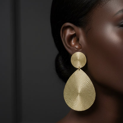 Gold earrings worn by a model against a dark background