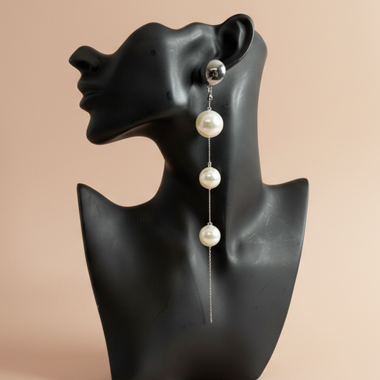 Pearl earring on a black mannequin bust against a beige background