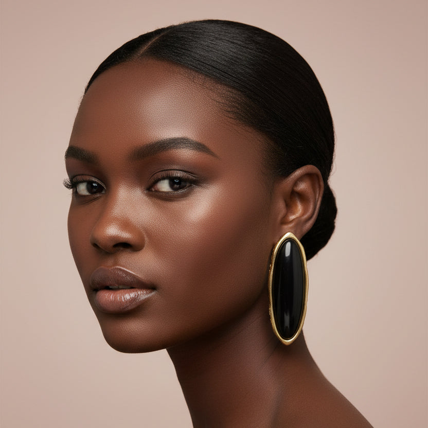 Woman wearing a black and gold large stud earring against a beige background 