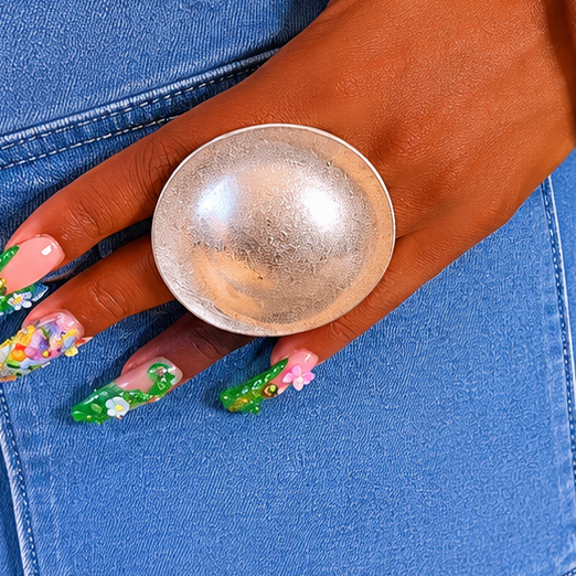 Hand wearing a large metallic ring with floral nail art on a blue denim background