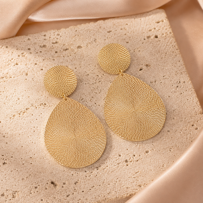 Gold textured earrings on a beige stone surface