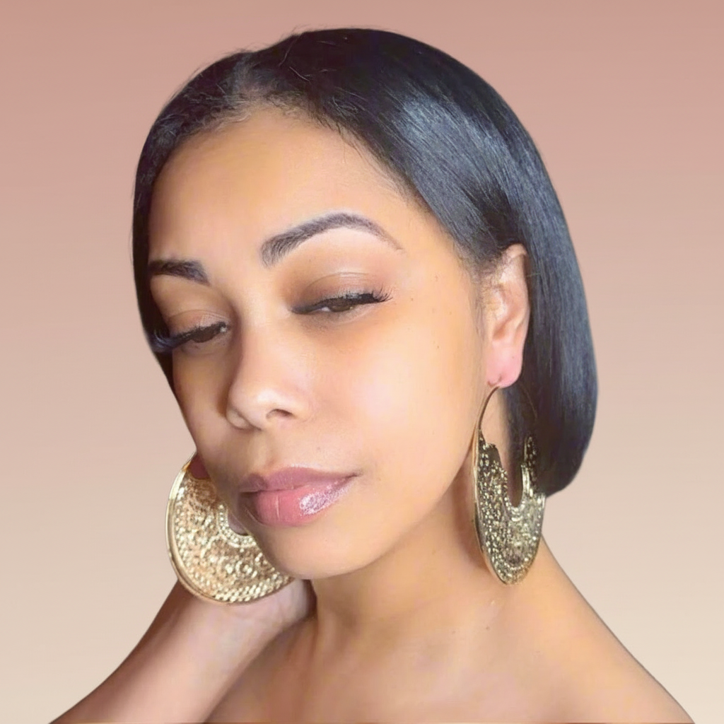 Woman wearing large gold hoop earrings against a neutral blush background