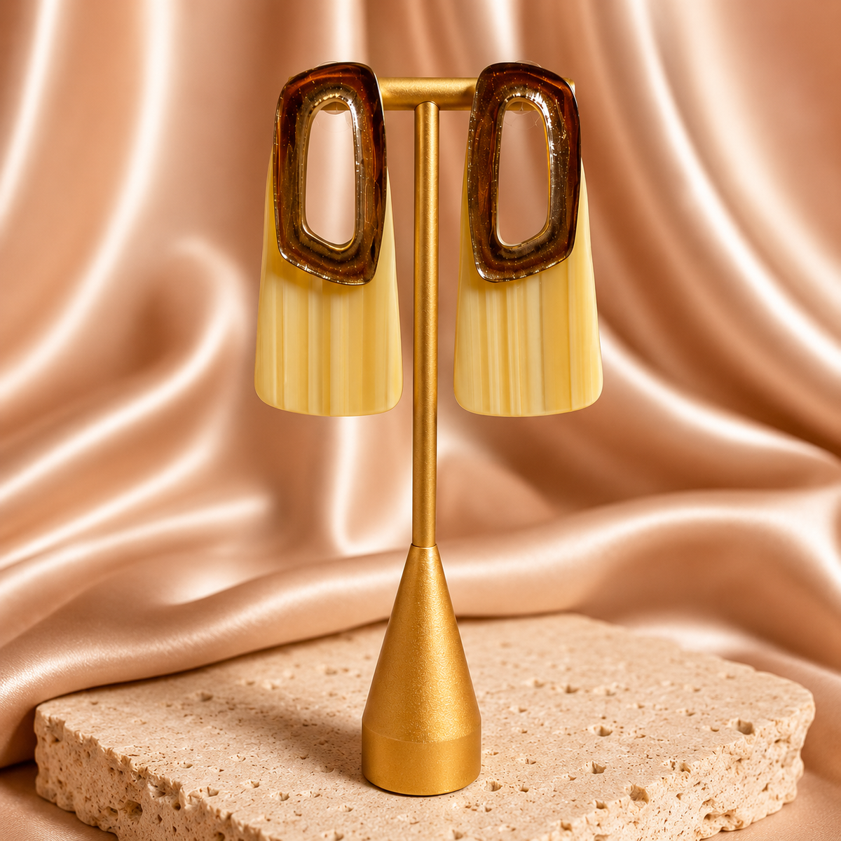 Gold earring stand with gold and peach earrings against a pink satin background