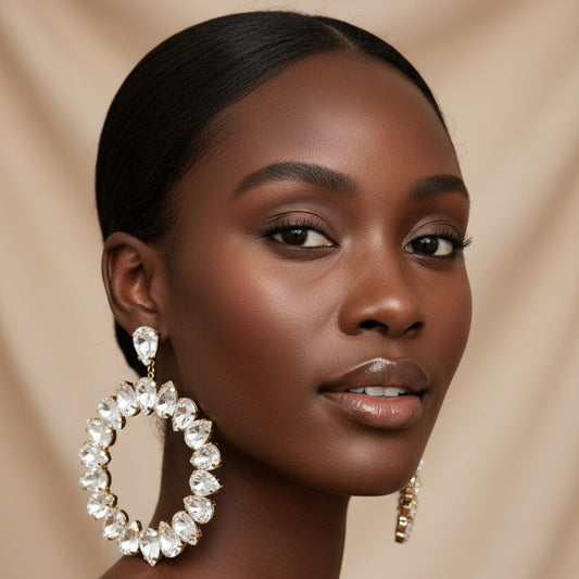 A woman wearing A pair of silver-tone hoop earrings adorned with clear rhinestones, displayed against a champagne background 