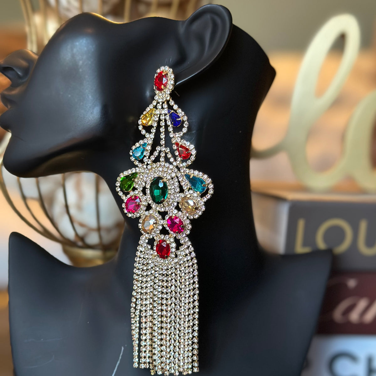 Decorative earring with colorful gemstones on a black mannequin head.