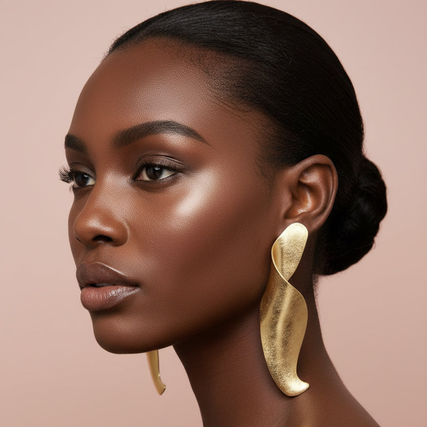 A woman wearing A large organic-shaped gold earring set against a nude background 