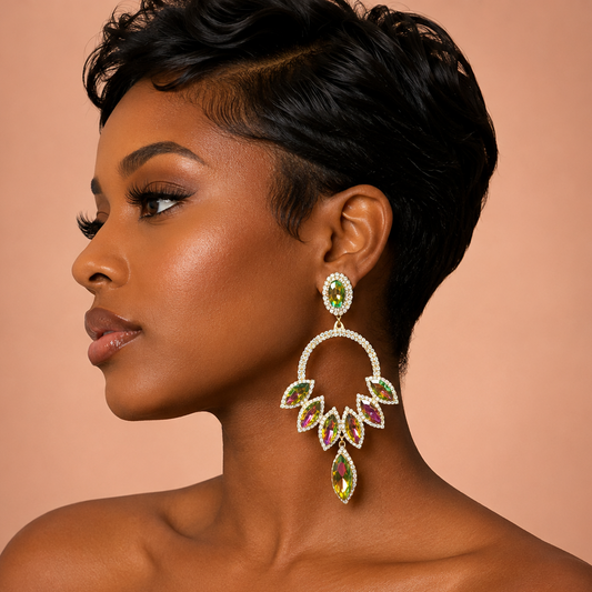 A woman in profile wearing a large, ornate gold-toned statement earring with green, pink, and yellow marquise-cut crystals, set against a solid peach background.