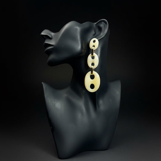 Pair of beige earrings on a black mannequin bust against a black background