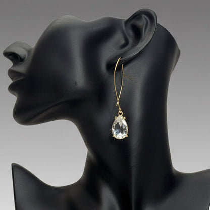 Gold earring with a clear teardrop-shaped gemstone on a black mannequin ear.