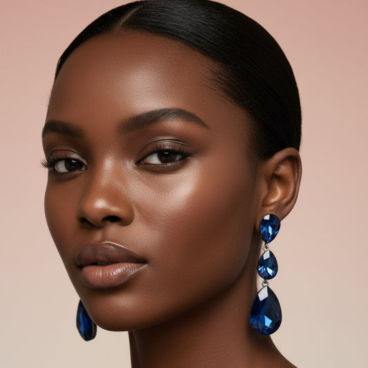 A woman wearing a pair of blue teardrop dangle earring displayed against a blush background 