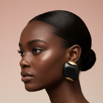 A close-up side profile of a woman with dark hair in a bun, wearing a large black and gold statement earring, set against a solid warm beige background.