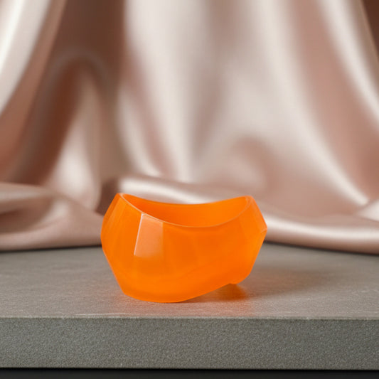 Orange resin bangle on a neutral slab against a blush satin drape 