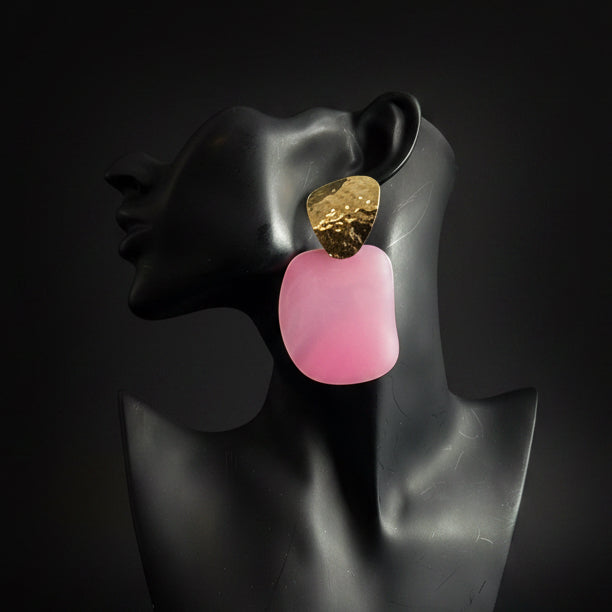 Black mannequin bust with pink and gold earring against a black background 