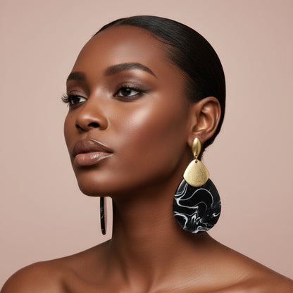 A woman wearing a pair of gold and black dangle earrings displayed against nude background 