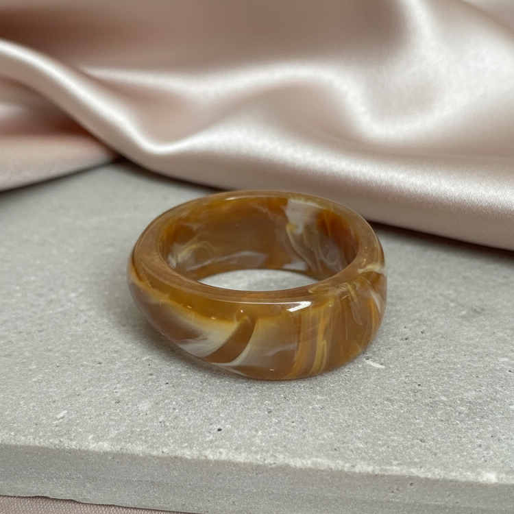 Marbled brown and white bangle on a textured surface with a pink satin fabric background