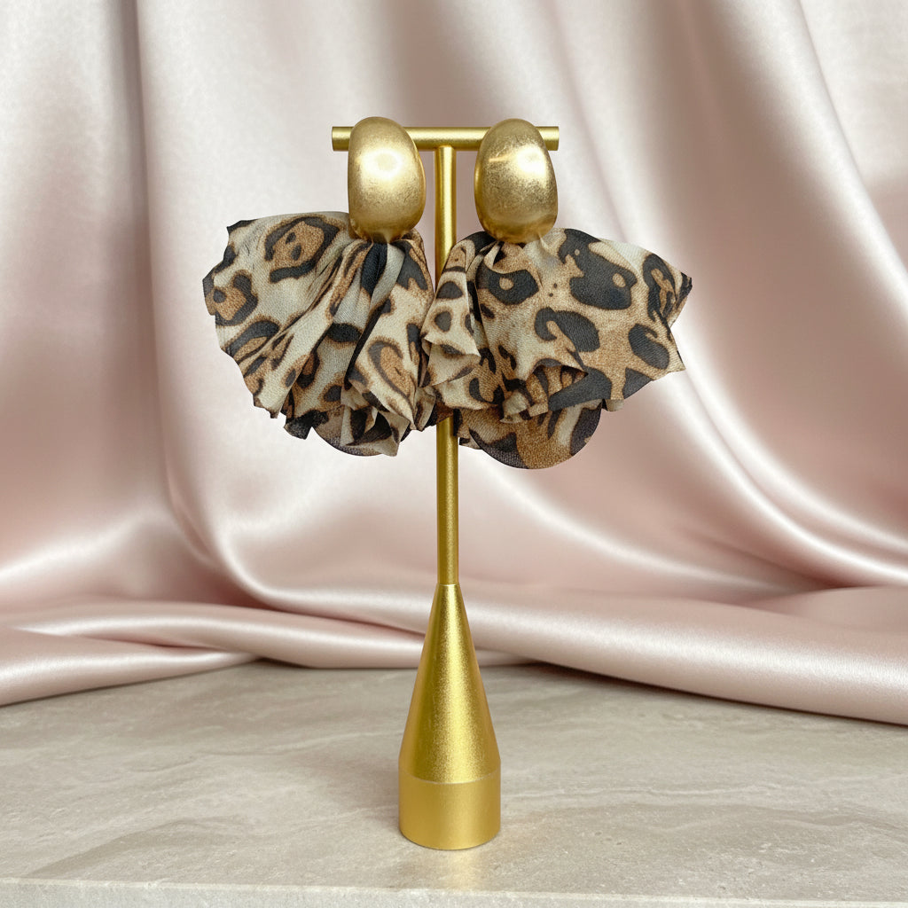 Leopard print earrings on a gold stand against a pink satin background