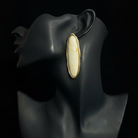 Gold and cream earring with a large central stone on a black mannequin head.