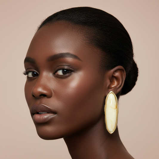 Woman wearing large gold and beige earrings against a beige background