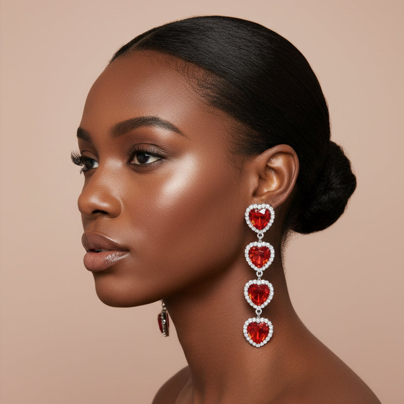 A woman wearing A pair of long drop earrings with four red heart charms outlined in silver, displayed against a nude background 