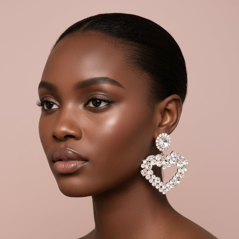 Woman wearing a large, clear and gold rhinestone heart-shaped earring on a beige background