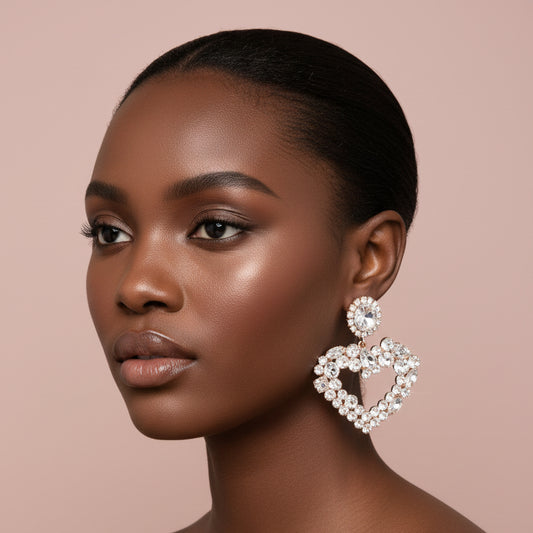Woman wearing a large, clear and gold rhinestone heart-shaped earring on a beige background