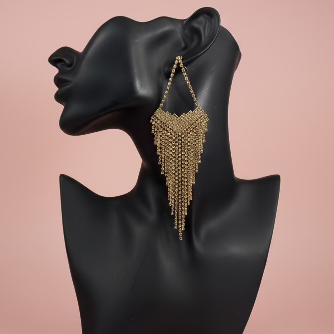 Gold beaded fringe earring on a black mannequin bust against a pink background